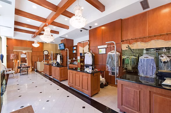 A dry cleaning shop interior with wooden counters, chandeliers, hanging garments in plastic, and tiled floor.