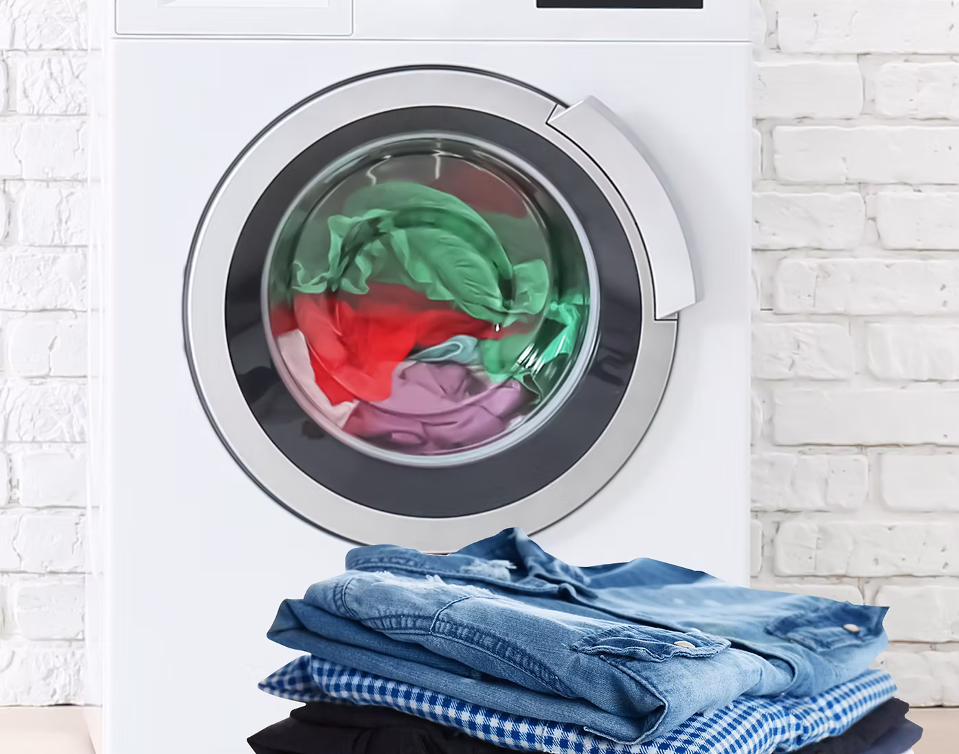 Front-loading washing machine with colorful clothes inside, and a neatly folded stack of jeans and shirts placed in front of it.
