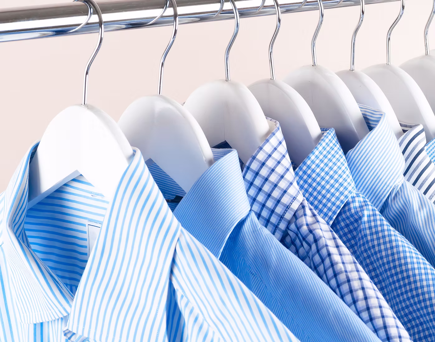 Several blue and white striped and checkered dress shirts hanging neatly on white hangers on a metal clothing rack.