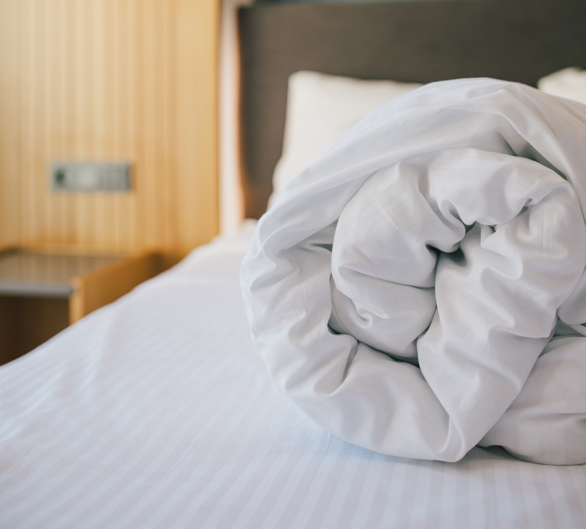 A rolled white comforter sits on a neatly made bed with white sheets in a modern bedroom.