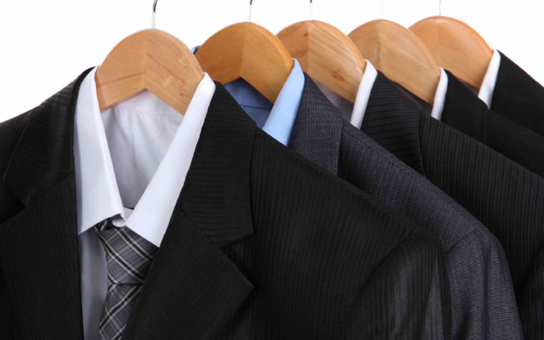 Four business suits with dress shirts and ties hanging on wooden hangers in a row.